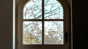 Une fenêtre à sommet en arc et au cadre blanc, donnant sur un arbre aux feuilles d’automne.