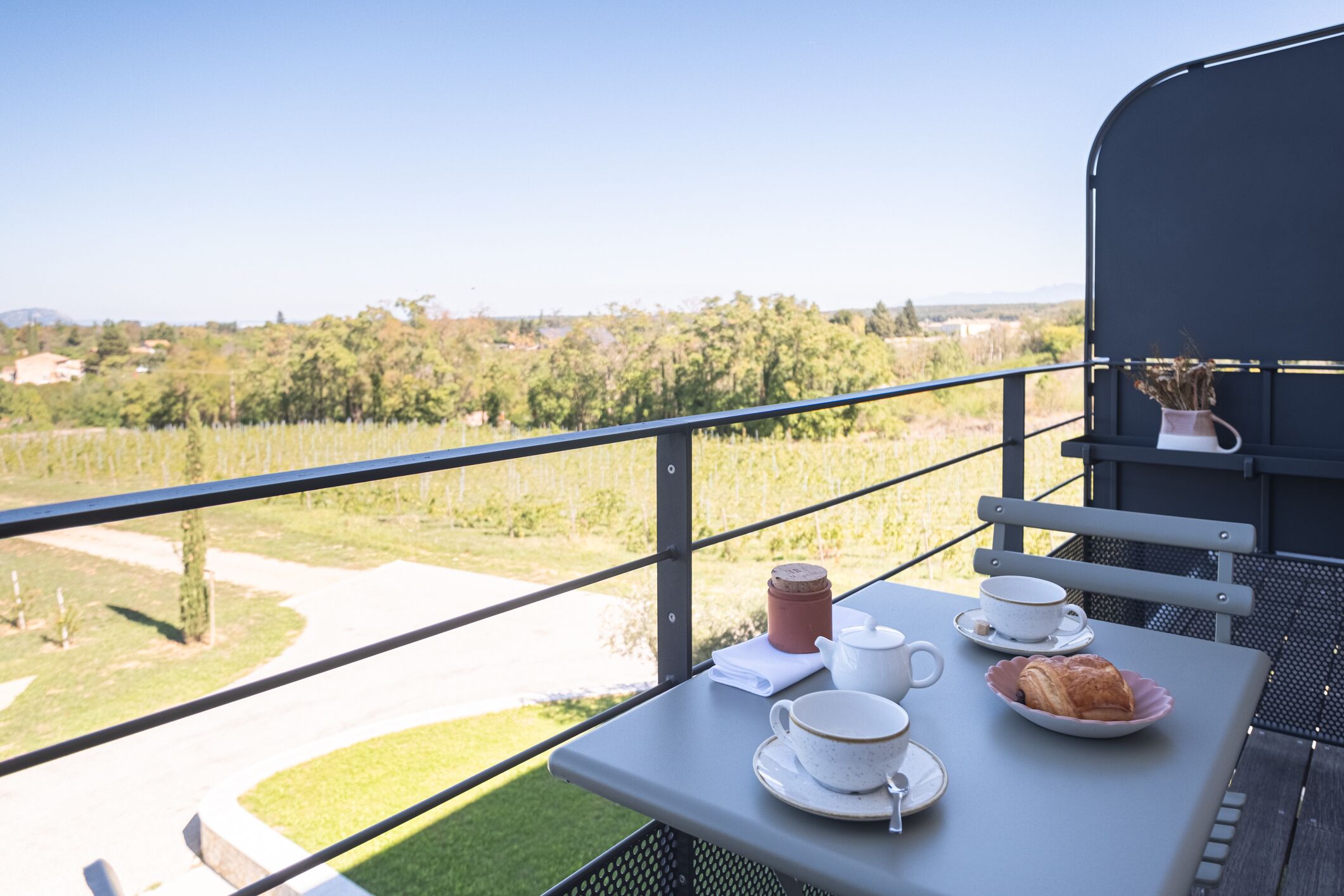 Un balcon avec une table préparée pour le thé, un croissant et un pot.