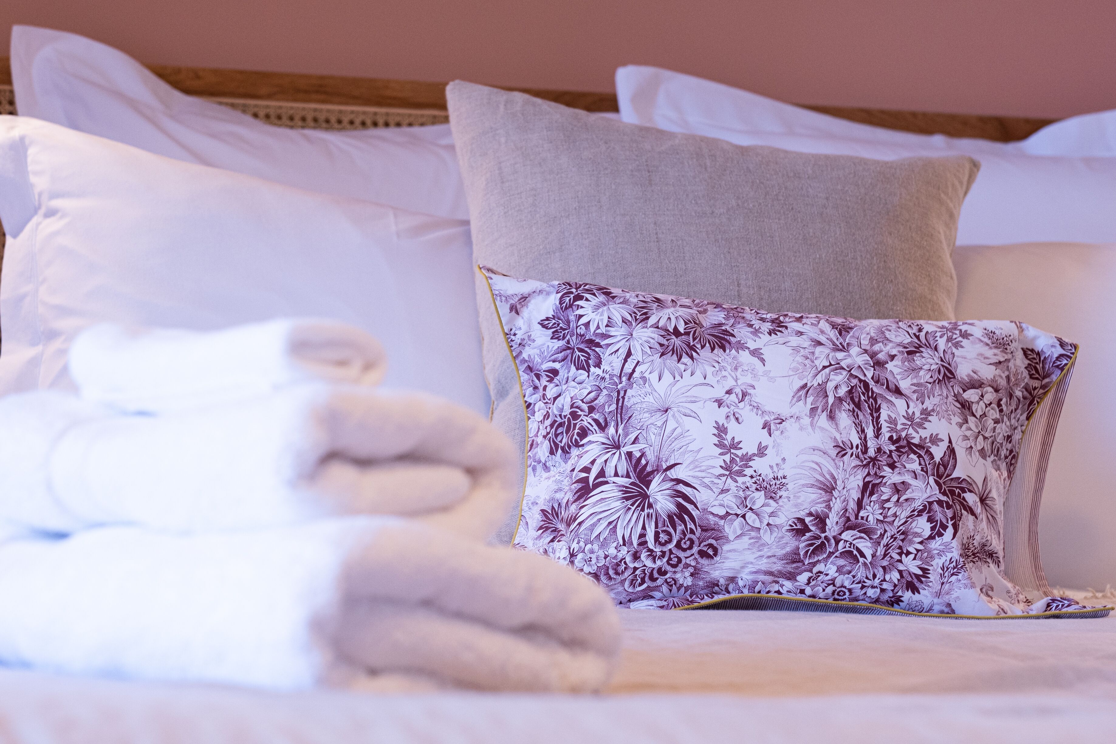 Cama bem arrumada com lençóis brancos e almofada estampada com flores.