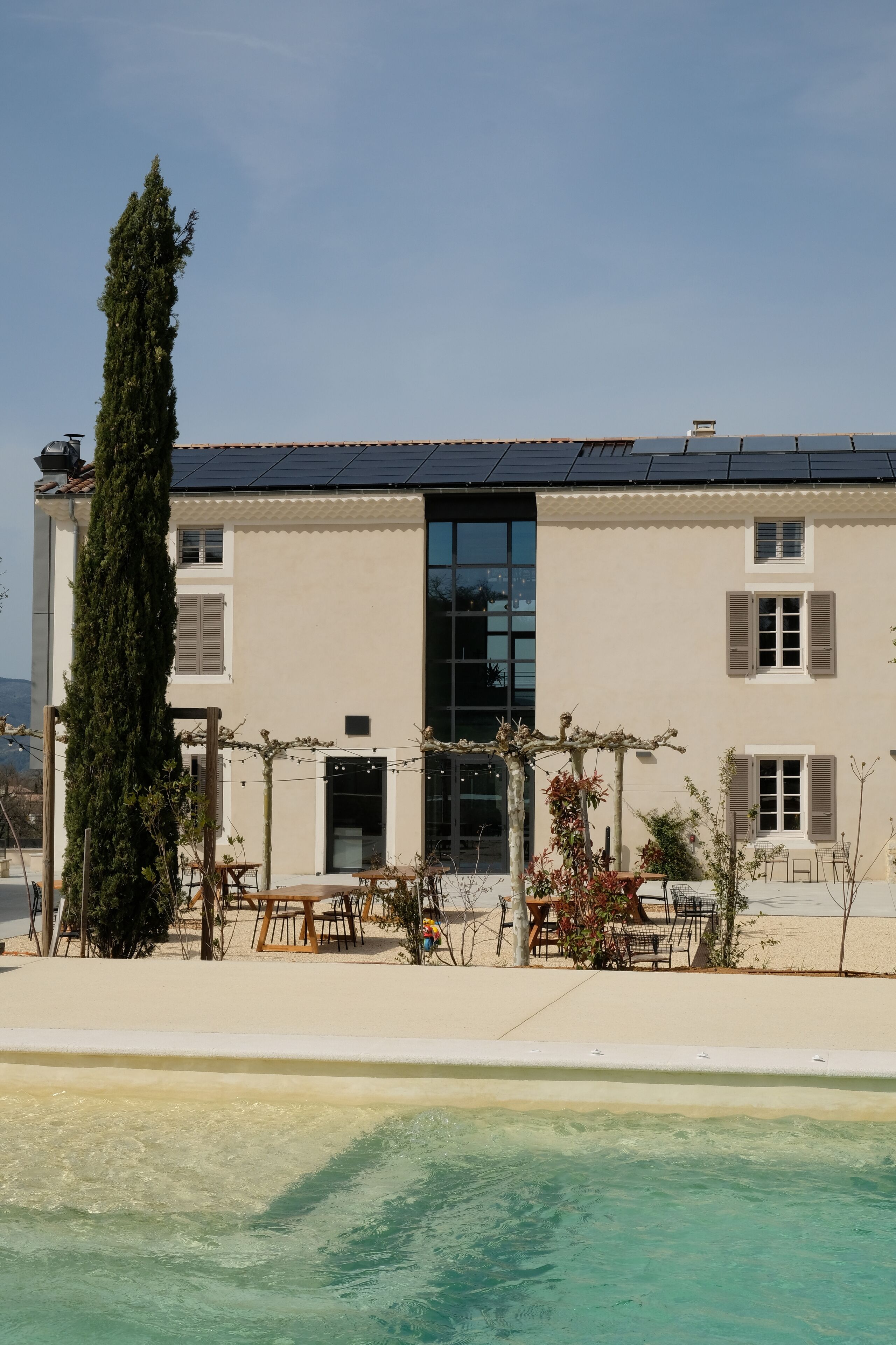 A two-story building with a flat roof, large windows, and a swimming pool in the foreground.