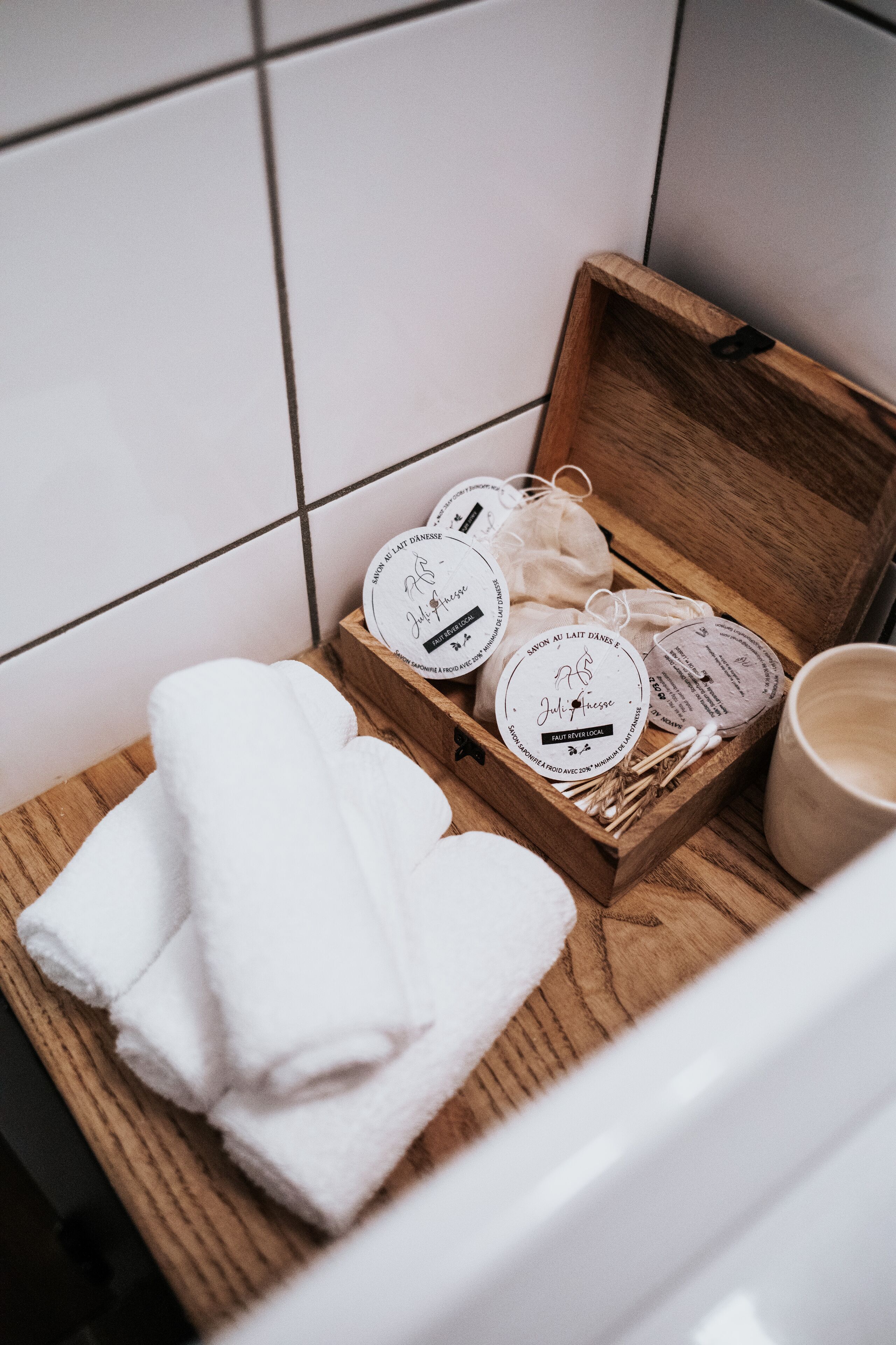 A wooden box with white towels and a mug on a tiled surface.