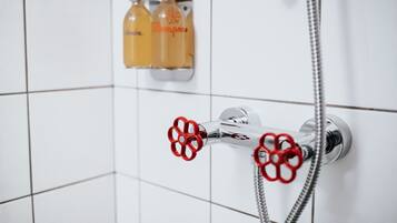 Una ducha con grifo cromado y mandos de color rojo, además de dos botellas de champú en la pared.
