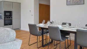 Ett modernt kök med inbyggda vitvaror, en matplats med ett bord för fyra personer och en grå soffa i vardagsrummet.