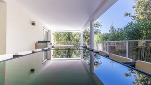 A modern balcony with a glass barrier, outdoor seating, and a view of greenery. - Villa PAPANO Pontaillac (Royan)