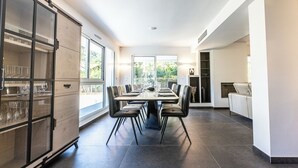 A modern dining area with a large table, chairs, and a cabinet with glassware. - Villa PAPANO Pontaillac (Royan)