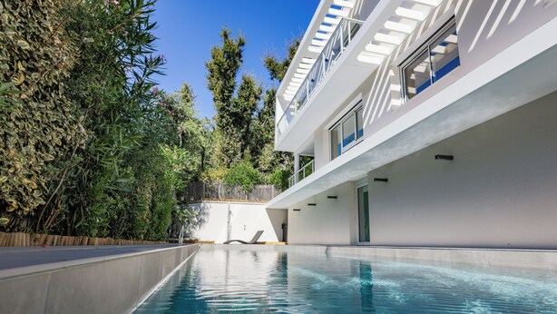A modern pool area with a clear pool, a white building with balconies, and dense greenery. - Villa PAPANO Pontaillac (Royan)