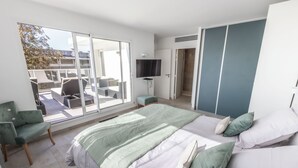 A bedroom with a large bed, a TV, and a balcony with outdoor furniture. - Villa PAPANO Pontaillac (Royan)