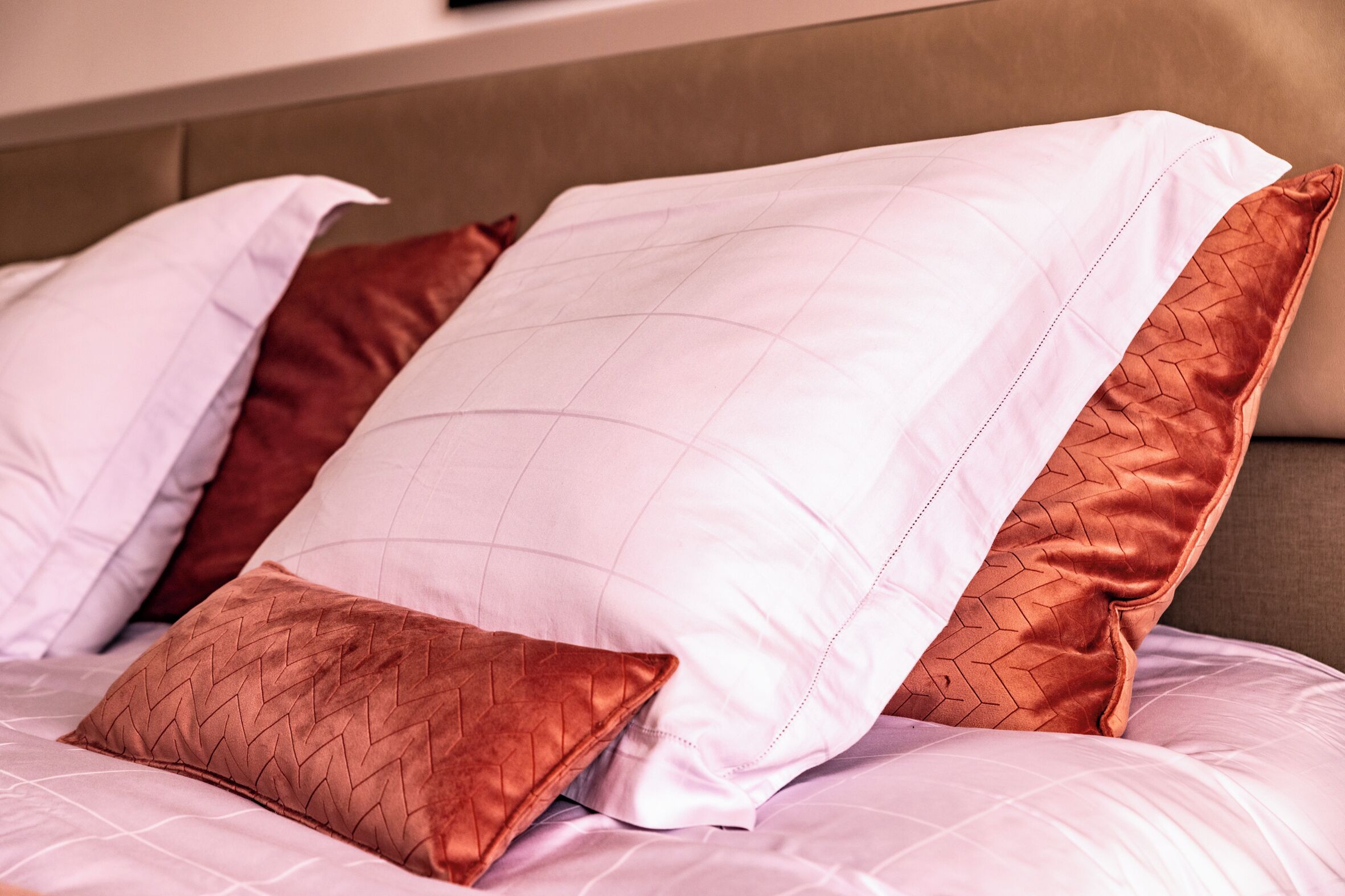Een bed met witte en bruine kussens, een hoofdbord en een bruine muur.