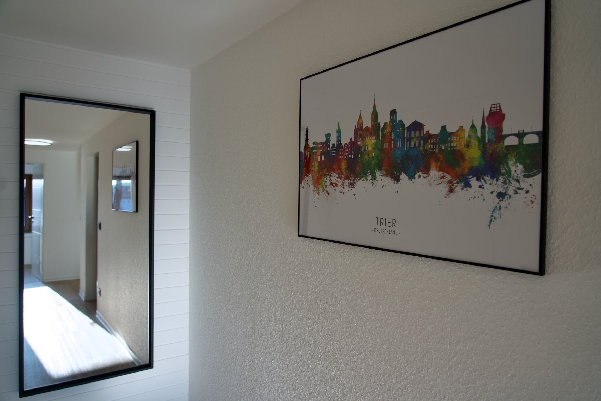 Een gang met een kunstwerk van een stadsgezicht en een spiegel.