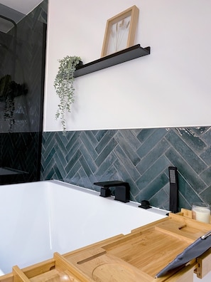 A modern bathroom with a large bathtub, a wooden shelf with a plant, and a herringbone-patterned tile backsplash. - Trimosa Apartment | Cozy, Bright, and Modern Apartment Near Trier (Trierweiler)