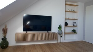 Una sala de estar moderna con un televisor de pantalla plana grande montado en una consola de madera, estantes de madera con plantas y un ventilador de techo.