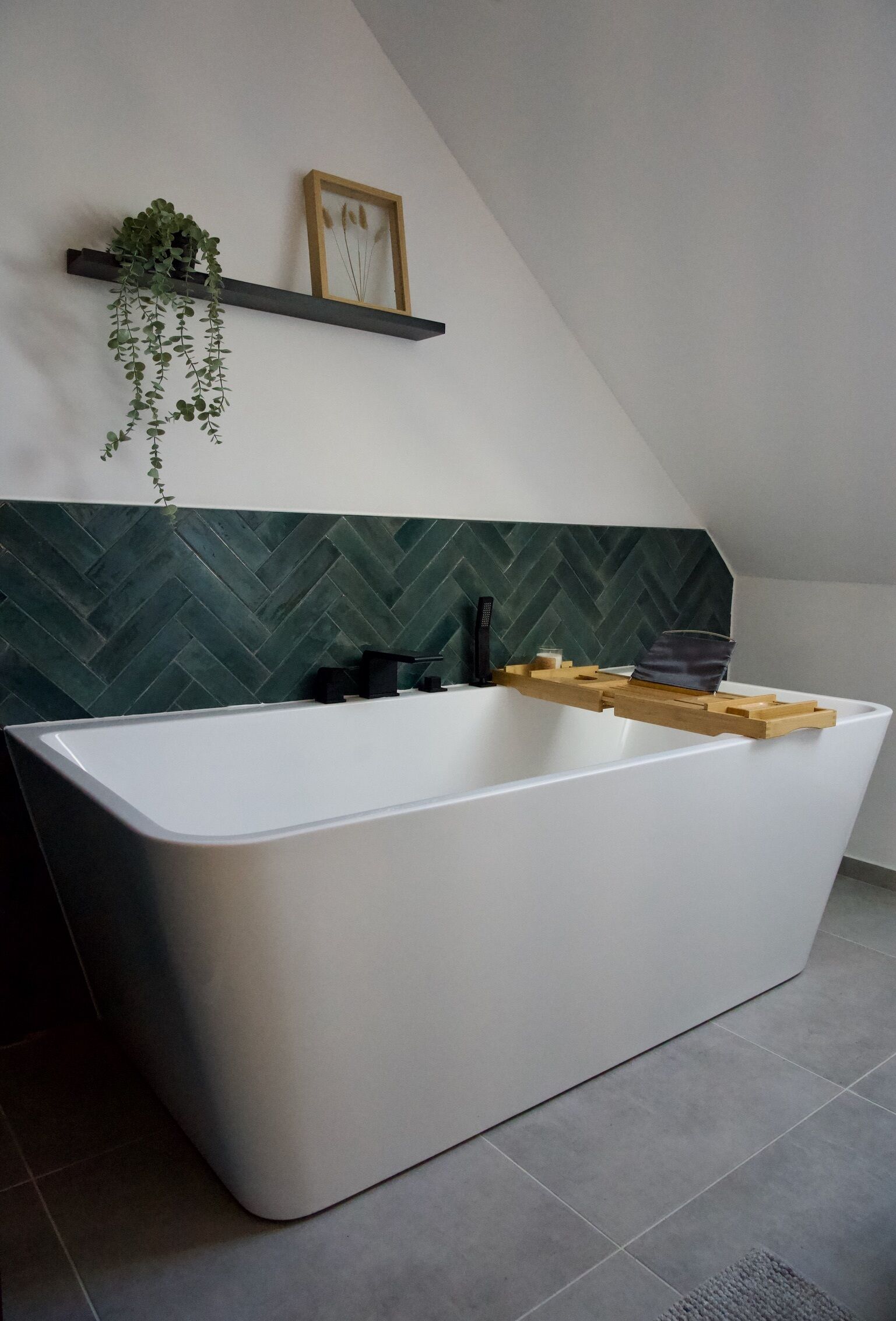 A modern bathroom with a freestanding bathtub, a wooden shelf with a plant, and a herringbone-patterned wall.