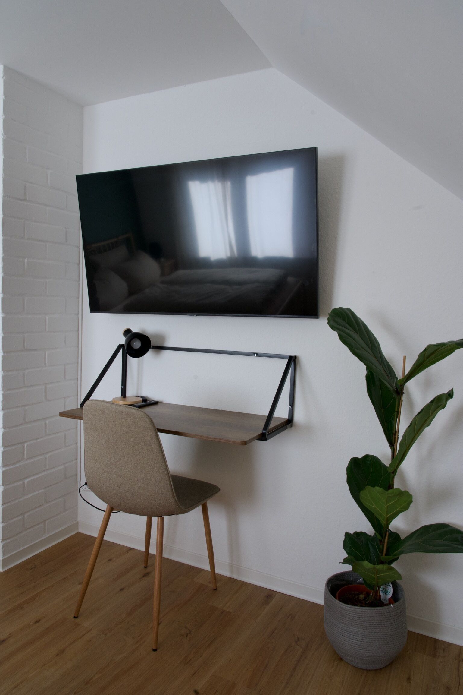 A modern room with a mounted TV, a desk with a chair, and a potted plant.