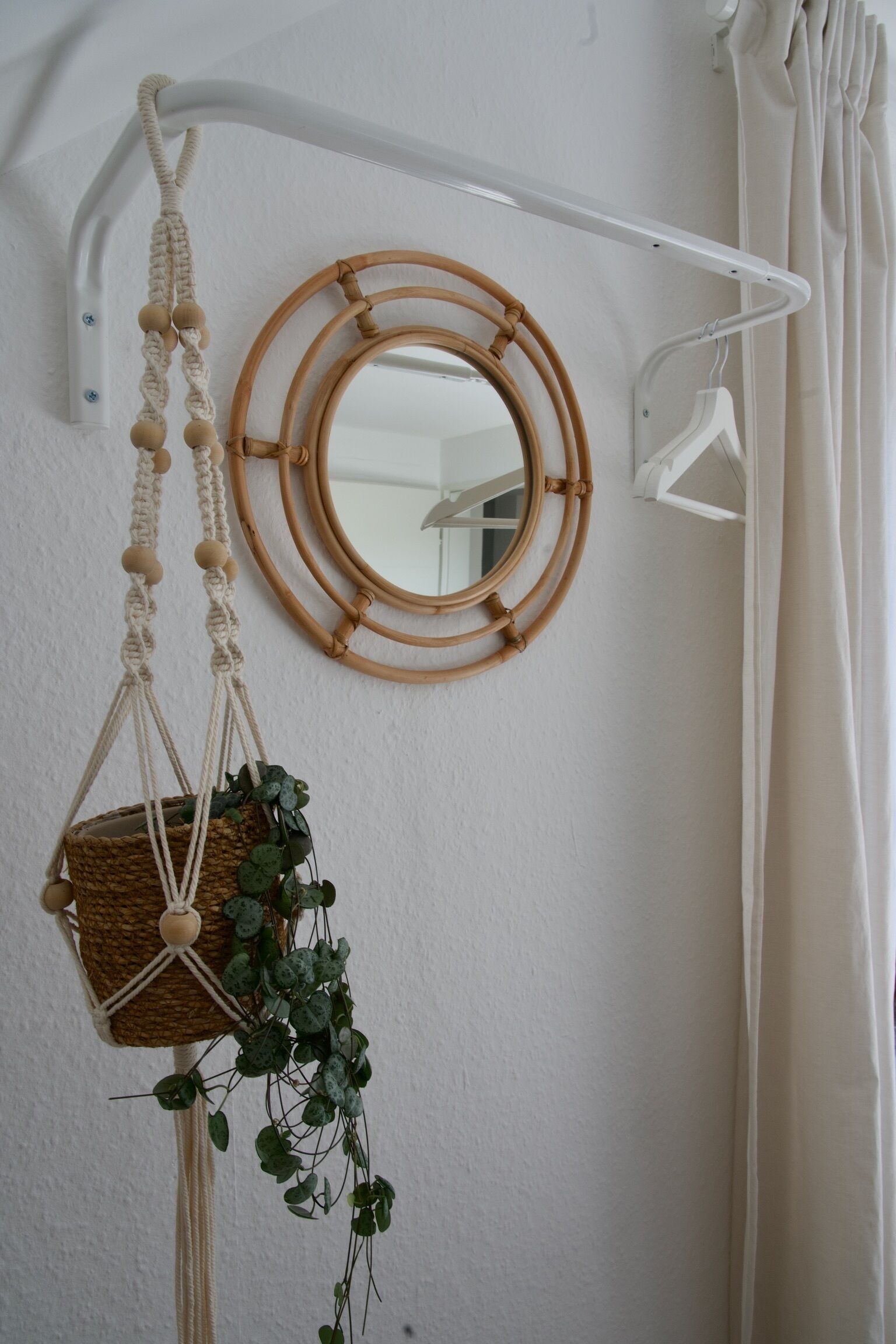 A wall-mounted mirror with a circular frame, a macrame wall hanging with a basket, and a white curtain.