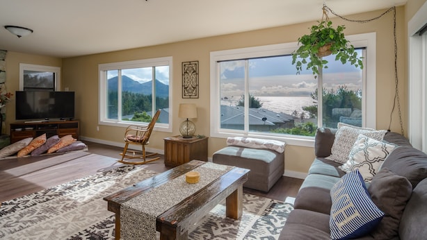 A living room with a large window, a television, a sofa, a coffee table, and a hanging plant. - Cannon Beach with Ocean Views, Dream Kitchen Made for Sharing, Spacious Deck, and Dogs Welcome (Cannon Beach)