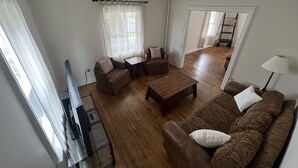 A living room with a brown sofa, two armchairs, a coffee table, and a TV. There is a window with sheer curtains and a door leading to another room. - Charming 4 BD near DT Geneva (Geneva)