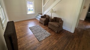 A spacious living room with hardwood flooring, a large window, a staircase, and two patterned armchairs. - Charming 4 BD near DT Geneva (Geneva)