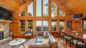 Ruime cabin met een groot houten interieur, een stenen open haard, een leren bank en een eethoek met een lange tafel.