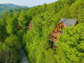 A cabin with a wooden exterior, elevated on stilts, surrounded by dense forest. - Ski In/Out @ Hatley Pointe ~Views~HotTub ~Fire Pit (Mars Hill)