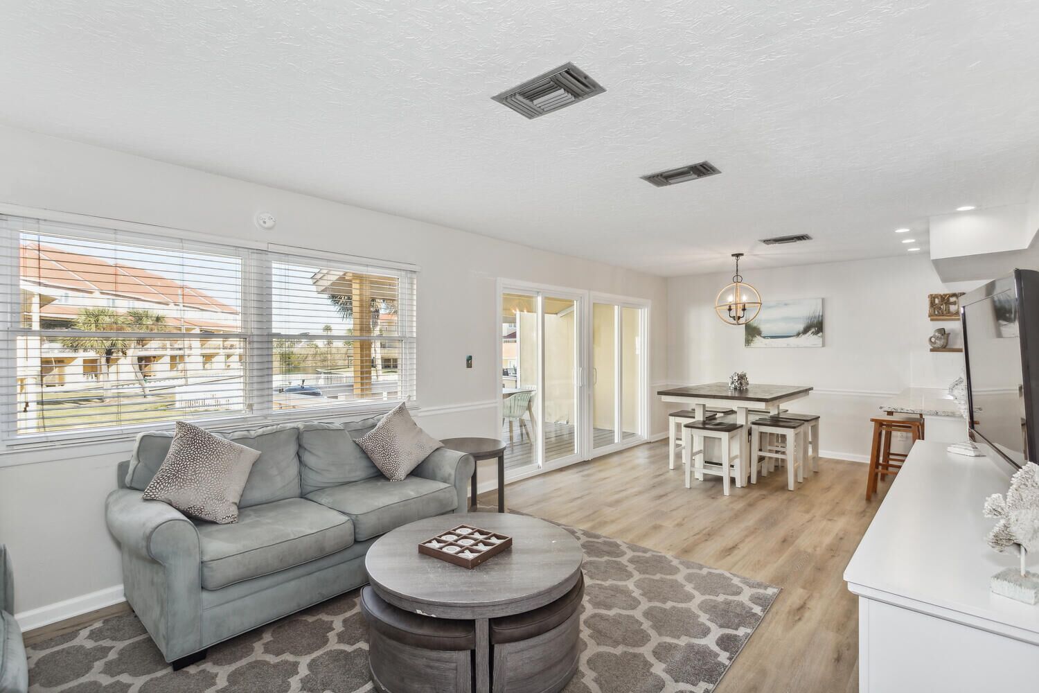 A modern living room with a grey sofa, a round coffee table, and a dining area with a white table and chairs.