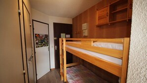 A small room with a bunk bed, wooden cabinets, a door with a colorful poster, and a white textured wall. - View open, balcony, parking, tv, ski locker, 27m², Auris en Oisans (Auris)