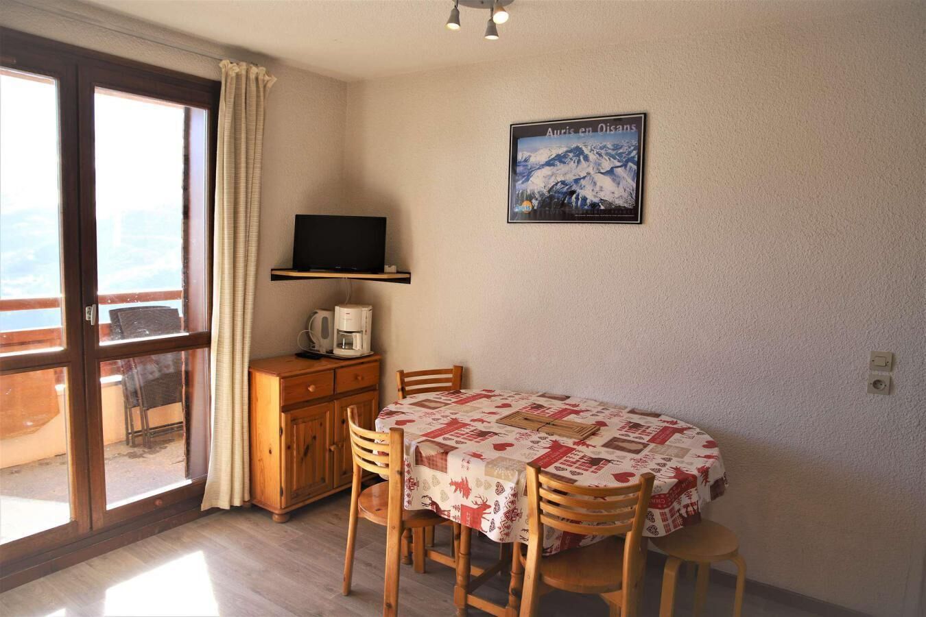 Een kamer met een houten tafel en stoelen, een televisie op een plank, een koffiezetapparaat en een ingelijst schilderij aan de muur.