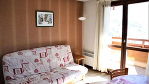 A cozy room with a patterned sofa, a small table, and a view of a balcony. - View open, balcony, parking, tv, ski locker, 27m², Auris en Oisans (Auris)