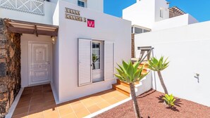 Une villa blanche dotée d’un patio carrelé, d’une porte et d’un petit jardin planté d’agaves.