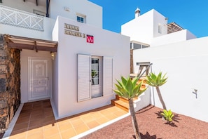 A white villa with a tiled patio, a door, and a small garden with agave plants. - Villa Calima by Villa Plus (Puerto del Carmen)