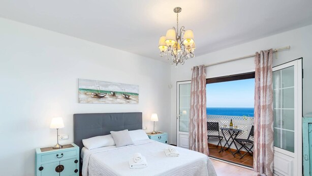 Une chambre à coucher avec un lit, des lampes de chevet, un tableau et un balcon équipé d’une table et de chaises.