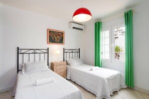 Une chambre avec deux lits, une table de chevet, une lampe, un tableau, un appareil de climatisation et une fenêtre avec des rideaux.