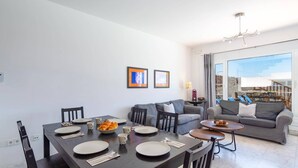 Un salon moderne avec un coin repas, des canapés gris et une grande fenêtre donnant sur un beau paysage.