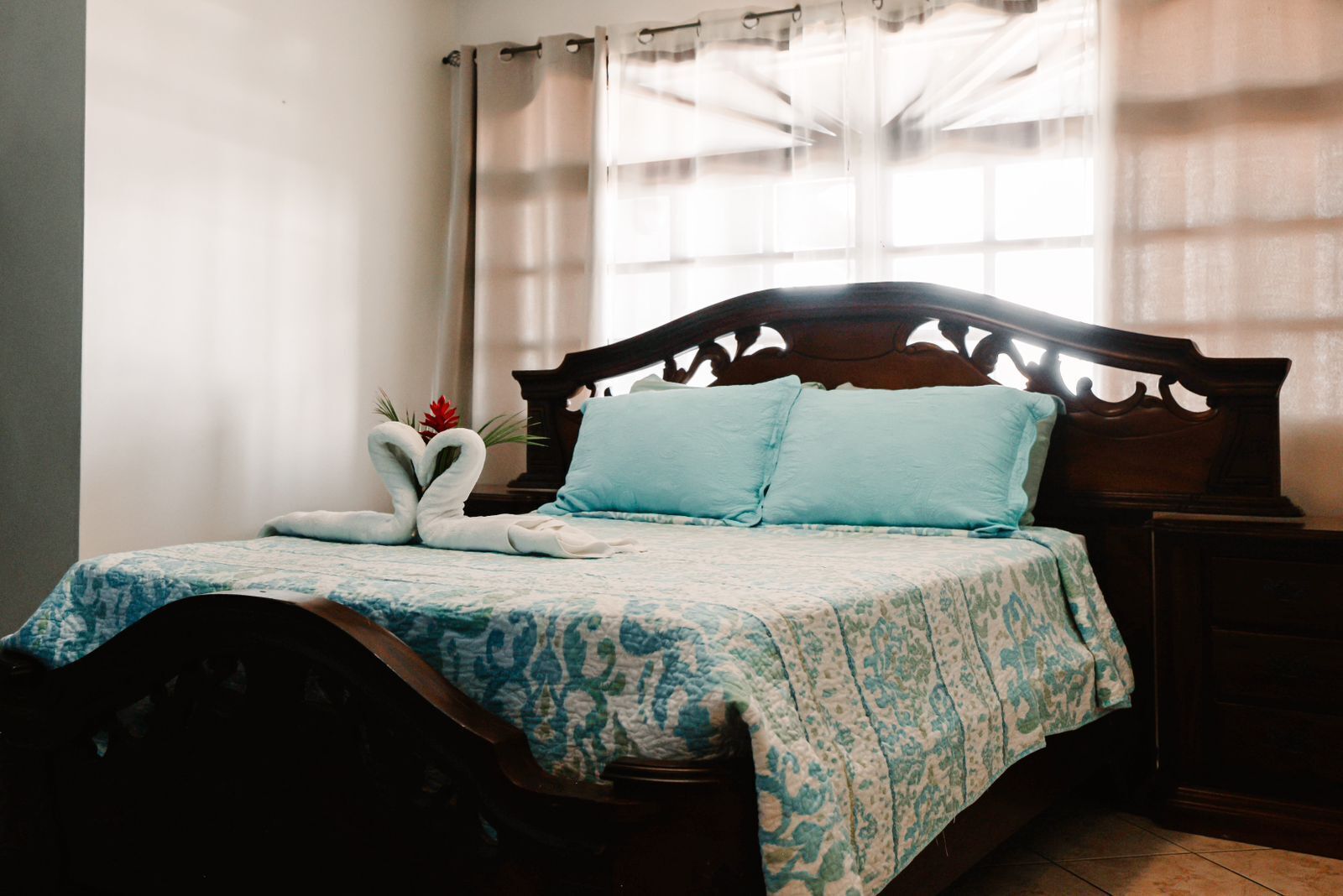 Un letto rifatto con cura, con una coperta a fiori, due cuscini e un’elegante composizione di asciugamani a forma di cuore.
