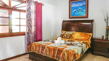 Un dormitorio con cama, cortinas, un cuadro y una mesita de noche.
