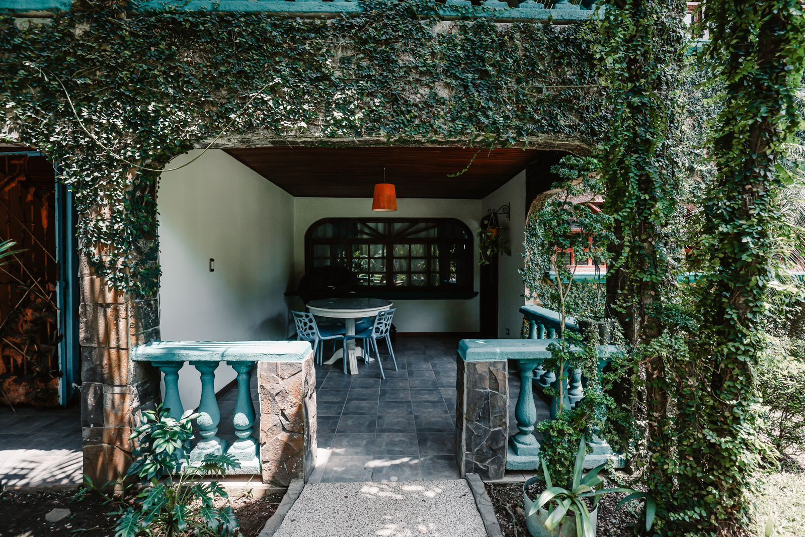 An outdoor seating area with a table and chairs, surrounded by greenery and a stone pathway.