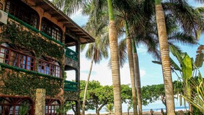 A two-story building with a balcony, surrounded by tall palm trees and lush greenery. - Casa de Playa - Playa Hermosa Jaco (Jacó)