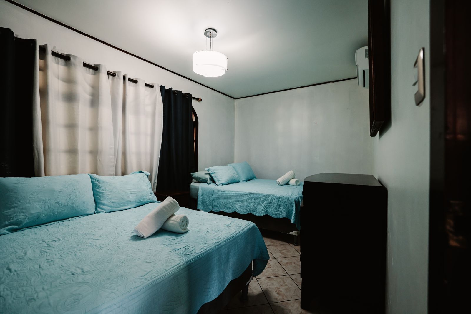 Ein Hotelzimmer mit zwei Betten, jeweils mit blauer Bettdecke und Kissen, einem kleinen Schreibtisch und einer Deckenleuchte.