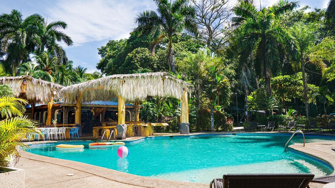 Piscina com espreguiçadeiras e uma estrutura com telhado de palha.