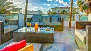 Une terrasse sur le toit, aménagée avec des meubles en osier, une table en verre et offrant une vue sur les immeubles et les palmiers.