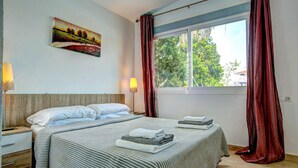 Une chambre d’hôtel avec un lit, une table de chevet, une lampe, une fenêtre avec des rideaux et un tableau au mur.