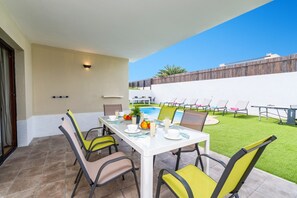 Un patio con una mesa dispuesta para cuatro personas, sillas alrededor y una piscina al fondo.
