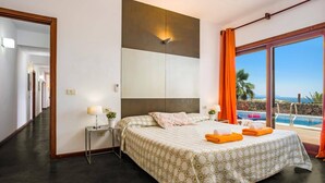 A hotel room with a bed, a nightstand, a lamp, a view of the ocean, and a pool. - Villa Corito Cinco by Villa Plus (Playa Blanca)
