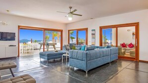 A spacious living area with a blue sofa, a dining table, and a TV mounted on the wall. - Villa Corito Cinco by Villa Plus (Playa Blanca)