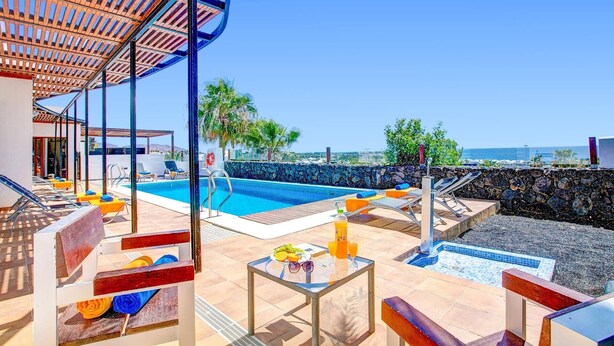 A pool area with lounge chairs and a table with drinks and snacks, overlooking a clear blue sky and a distant view. - Villa Corito Cinco by Villa Plus (Playa Blanca)