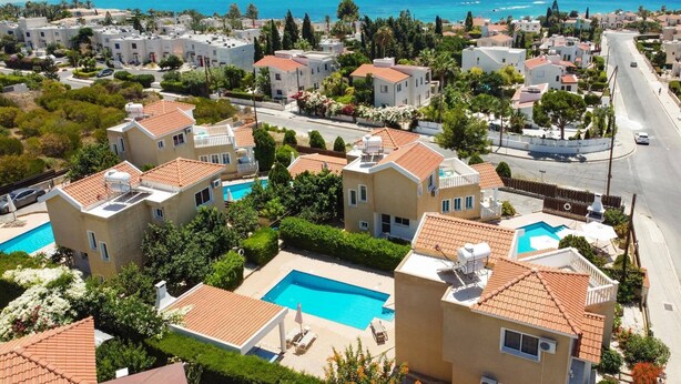 A coastal residential area with modern houses, a swimming pool, and a view of the sea. - Villa Camelia by Villa Plus (Peyia)