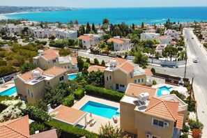 A coastal residential area with modern houses, a swimming pool, and a view of the sea.