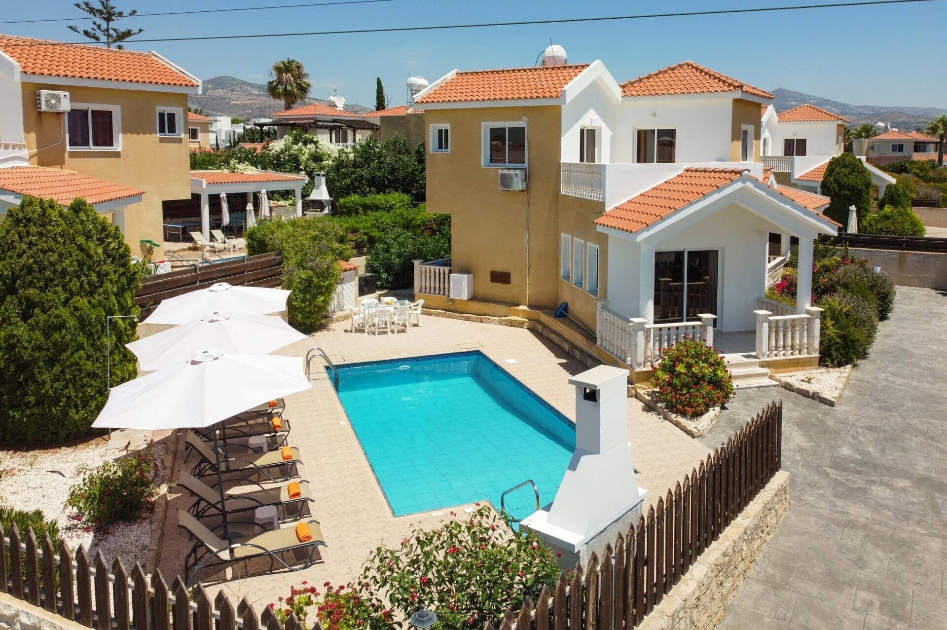 A residential area with a swimming pool, sun loungers, and a fenced patio.