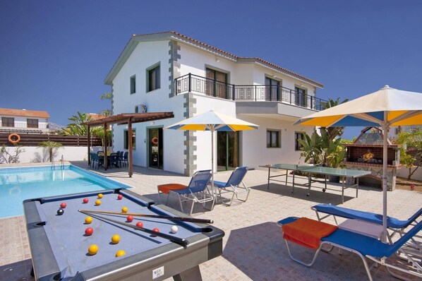 Un área de piscina con mesa de billar, sillones de descanso y sombrillas.