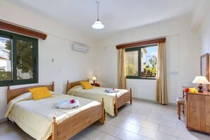 Una habitación con dos camas de madera, un ventilador de techo, una ventana con cortinas y un pequeño armario de madera.