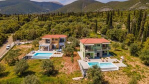 Une maison moderne à deux étages avec une piscine, entourée d’une végétation luxuriante et de montagnes.